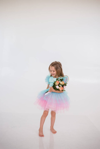 malá holčička v šatech s sukní tutu drží kytici čerstvých květin na bílém pozadí s místem pro text - Fotografie, Obrázek