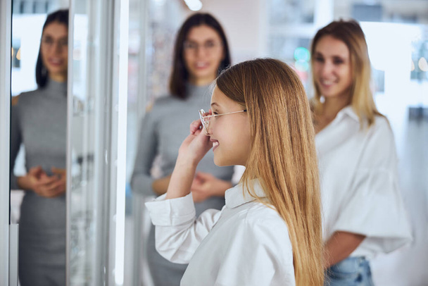 Happy uśmiechnięta nastolatka dziewczyna w białej koszuli patrząc na lustro w pokoju wewnątrz - Zdjęcie, obraz