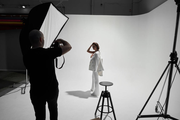 Fashion photography in a photo studio. Professional male photographer taking pictures of beautiful woman model on camera, backstage - Foto, immagini