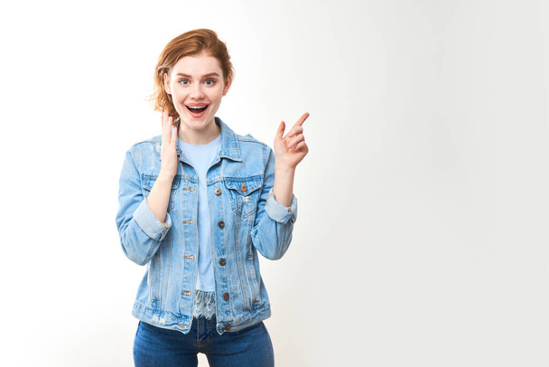 Portrait of a young red-haired girl on a white isolated background in jeans. Looks into the camera - Foto, afbeelding