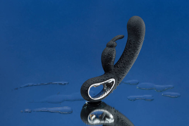 Black vaginal vibrator in drops of water hanging in the air on a dark blue background. Rabbit dildo with vibration. Space for text. Image for the sex shop. Sex toys for adult. - Фото, зображення