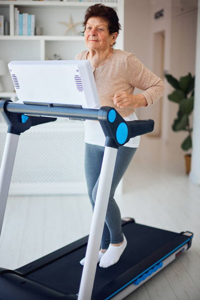 active mature woman running on treadmill at home, sporty lifestyle, 84 years old lady - Valokuva, kuva