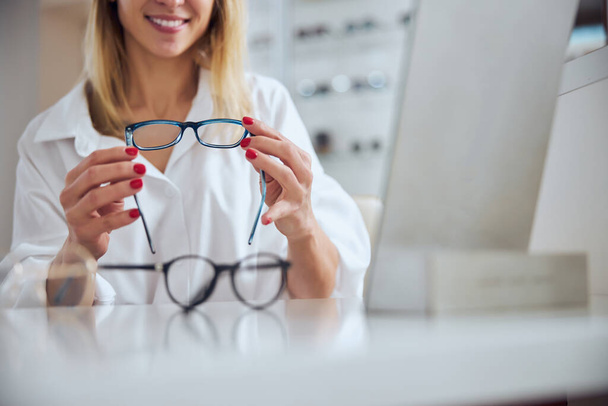 Beyaz bluzlu zarif bir kadın göz hekimliği kliniğinde gözlük için yeni lensler seçiyor. - Fotoğraf, Görsel