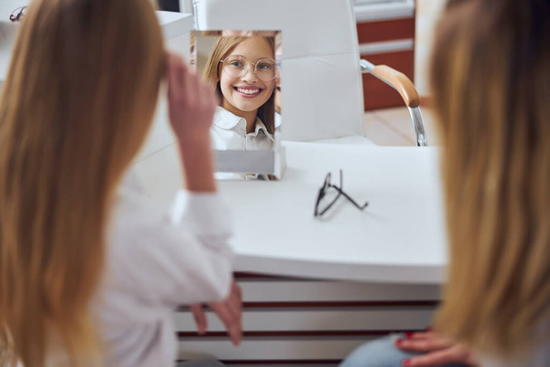 Щаслива усміхнена школярка в стильних окулярах в оптичному магазині
 - Фото, зображення