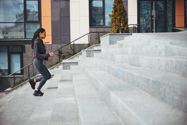 Sportswoman with trendy Afro bunches ascending the concrete steps - Fotó, kép