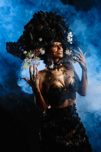 Portrait of a model in a headdress and dress made of coal. There is blue smoke behind the model. - Foto, Imagem