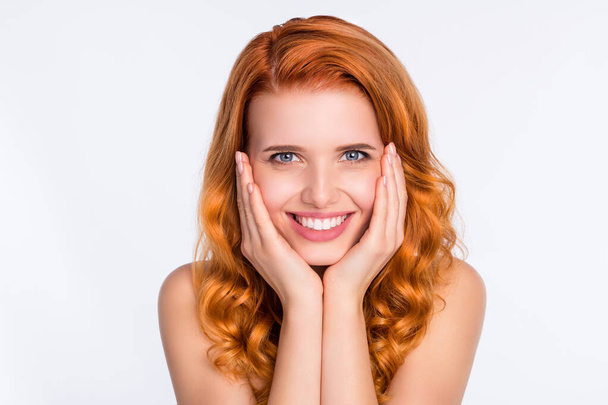 Φωτογραφία πορτρέτο του όμορφου κοριτσιού με σγουρά κόκκινα μαλλιά χαμογελώντας αγγίζοντας τα μάγουλα κάνοντας διαδικασίες του δέρματος απομονώνονται σε λευκό φόντο χρώμα - Φωτογραφία, εικόνα