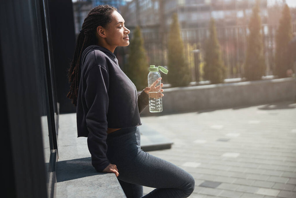 Thoughtful female with a plastic water bottle staring ahead - Φωτογραφία, εικόνα