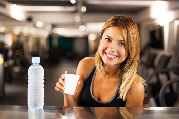 happy girl with bottle of water and a coffee cup resting in a generic out of focus fitness club - Valokuva, kuva
