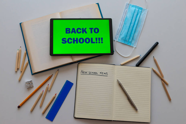 Tablet with "back to school" text, book, notebook, pen, pencil, template, crayons, pencils, ruler, on white surface. Beginning of schools and back to school; distancing and e-learning. New school year.  - Foto, imagen