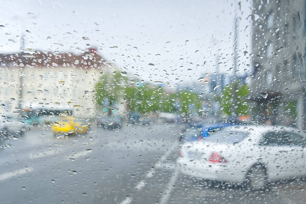 Auto guida in una tempesta di pioggia con vista sulla città offuscata. Vista dall'auto durante il giorno di pioggia - Foto, immagini