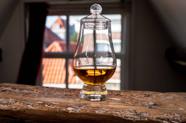 Drag of Single Malt Scotch Whisky serviert im Verkostungsglas mit Blick auf alte Fenster und Häuser auf Holzbalken - Foto, Bild