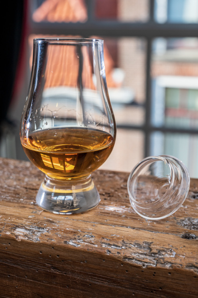 Dram z jedné sladové skotské whisky podávané v degustačním skle s výhledem na staré okno a domy na dřevěném trámu - Fotografie, Obrázek