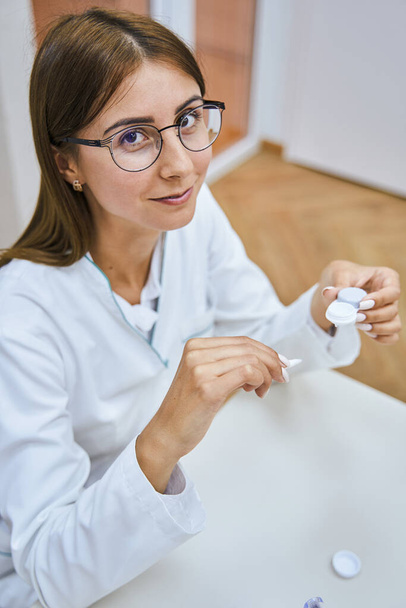 Charming young woman ophthalmologist holding contact lenses - Photo, image