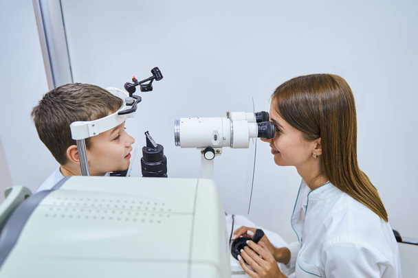 Vrouwelijke arts onderzoekt kinderogen met oogheelkundige apparatuur - Foto, afbeelding