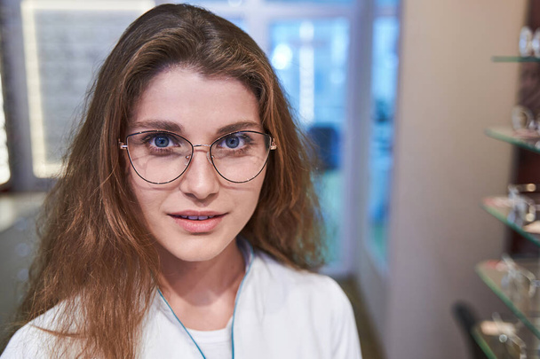 Bájos fiatal nő szemüvegben áll az optikai boltban - Fotó, kép