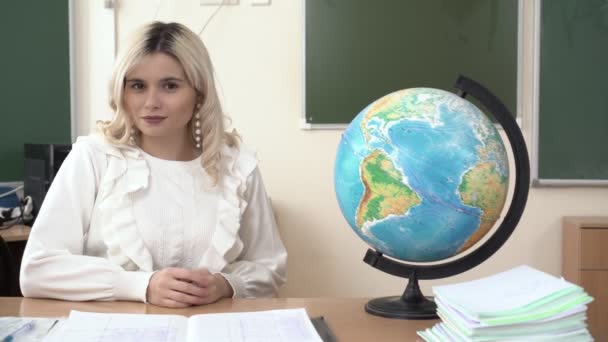 Portret van een jonge schoolleraar aan tafel in de klas met een wereldbol - Video