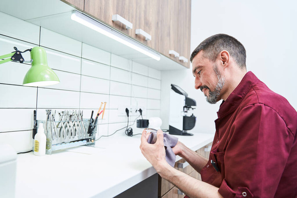 Mannelijke opticien reinigingslens voor bril in werkplaats - Foto, afbeelding