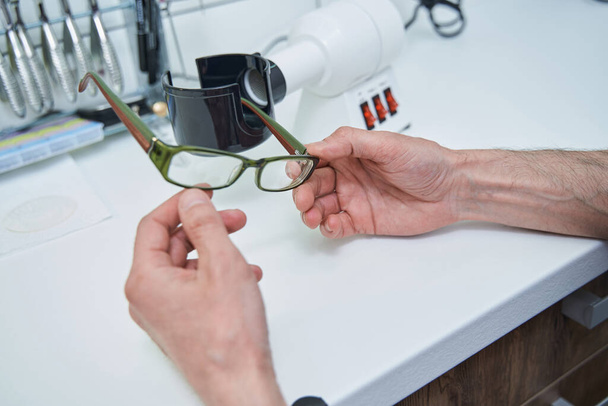 Mannelijke opticien handen met bril met groen frame - Foto, afbeelding