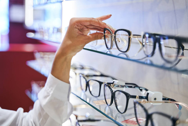 Női kéz, szemüveget vesz le a polcról az optikai boltban. - Fotó, kép