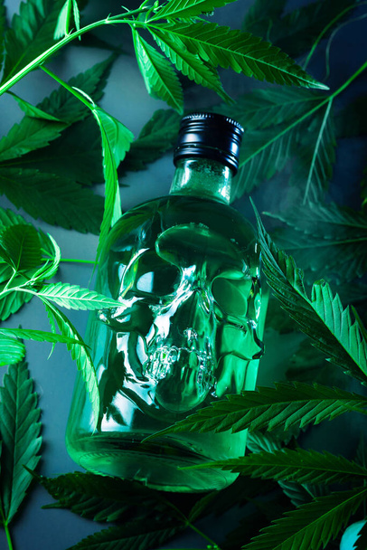 bottle in the shape of a human skull with a green drink with cannabis ruderalis leaves - Foto, Imagen