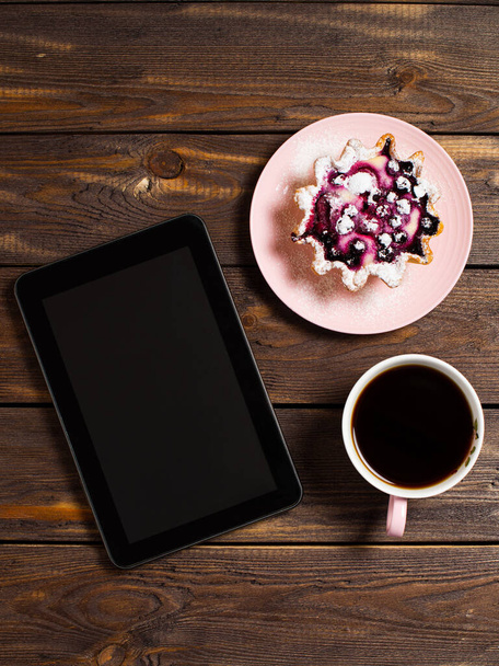 Flatley coffee break layout. Digital tablet gadget, black coffee in a cup and a cake basket with berries on a table from an old dark wood. - Photo, image