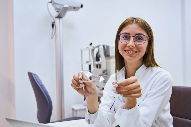 Χαρούμενη γυναίκα οπτικός με γυαλιά κάθεται στην ιστορία στην κλινική - Φωτογραφία, εικόνα