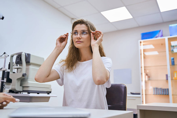 Bájos fiatal nő, szemüveget próbál az optikus irodában - Fotó, kép
