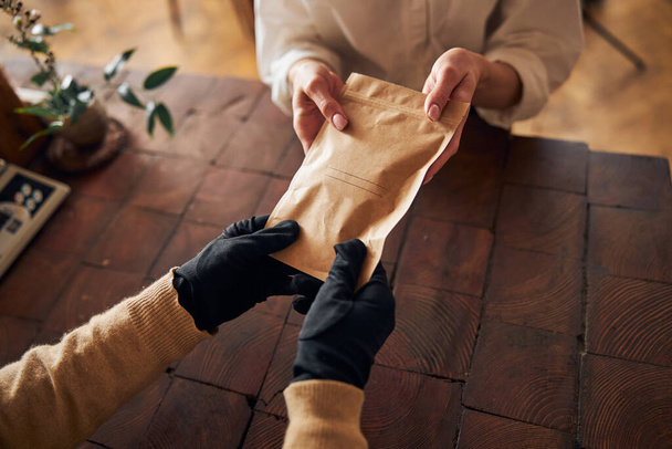 Mannelijke handen geven papieren zak aan jonge vrouw - Foto, afbeelding