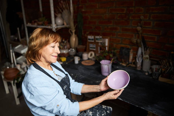 Charmante vieille femme tenant bol peint dans un atelier de poterie - Photo, image