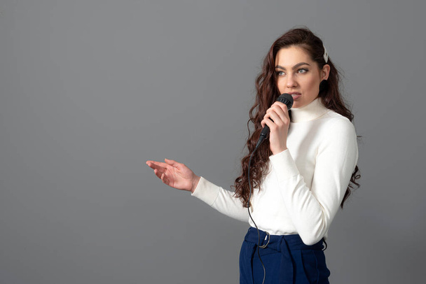 attractive female conference speaker during presentation, holds microphone and makes some gestures, isolated on gray - Fotografie, Obrázek