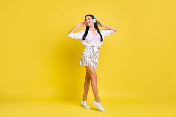 Full size photo of happy nice woman wear headset walk look empty space isolated on yellow color background - Foto, Imagen