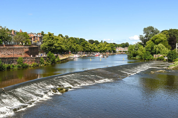 Chester, England - July 2021: Scenic view of boats on the River Dee, which flows through the city. In the foreground is a weir and fish pass. - Photo, Image
