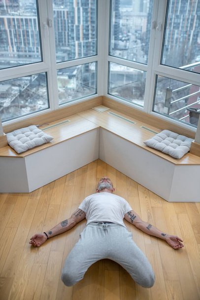 Gray-haired man in a white tshirt doing yoga and looking involved - Valokuva, kuva