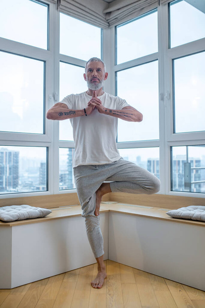 Gray-haired man in a white tshirt doing balance asana - Foto, Imagen
