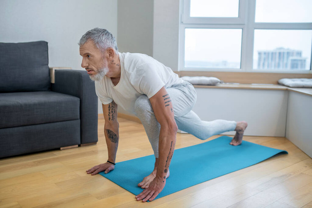A mature man practising yoga at home and looking concentrated - 写真・画像