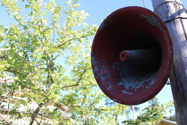 an old loudspeaker is hanging on a pole / photo of a street loudspeaker. it is attached to a post in the open air. the object is metal, old. the paint is peeling off. - Photo, Image