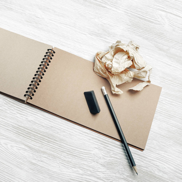 Foto de cuaderno kraft, lápiz, borrador y papel arrugado sobre fondo de mesa de madera clara. - Foto, Imagen