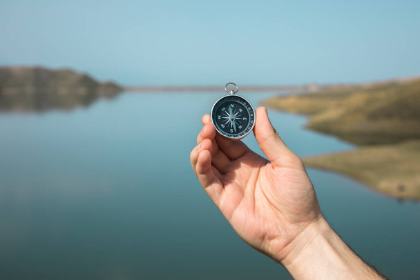 man hand holding compass in lake backgroun - Fotoğraf, Görsel