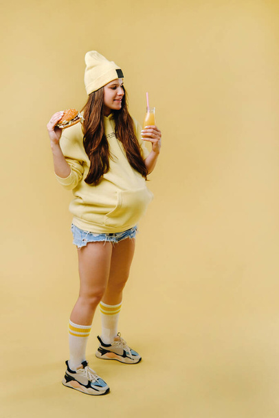 pregnant girl in yellow clothes with hamburgers in her hands on a yellow background. - Foto, immagini