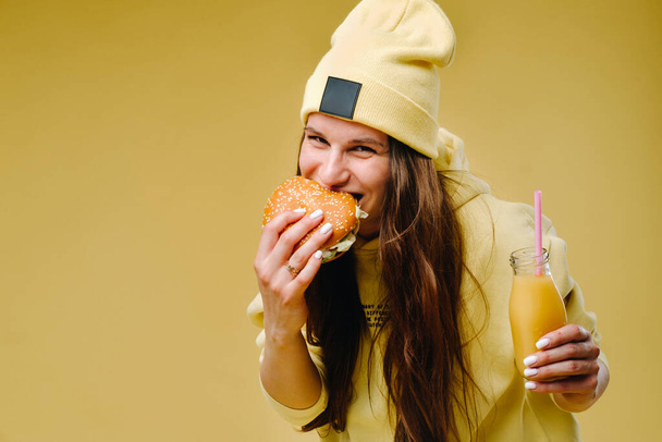 pregnant girl in yellow clothes with hamburgers in her hands on a yellow background. - Foto, afbeelding