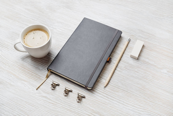 Foto van blanco schetsboek, potlood, gum en koffiebeker op lichte houten tafelondergrond. Stationaire modelbouw. - Foto, afbeelding
