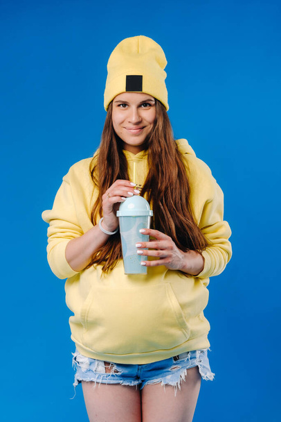 pregnant girl in yellow clothes with a glass of juice on a blue background. - Foto, Bild