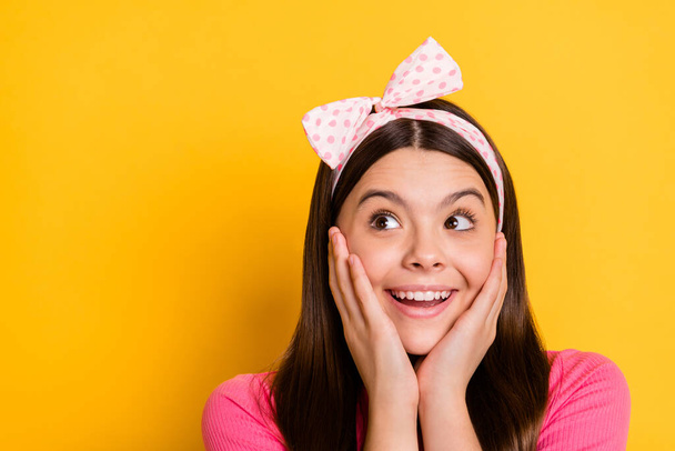 Photo of excited cute small schoolgirl dressed pink t-shirt arms cheekbones looking empty space isolated yellow color background - Φωτογραφία, εικόνα