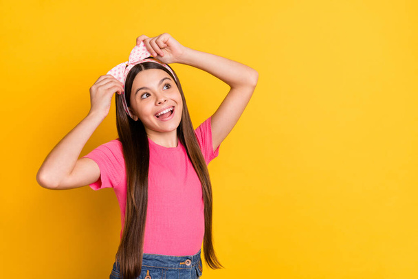 Photo of cute charming school girl wear pink t-shirt arms band looking empty space smiling isolated yellow color background - Φωτογραφία, εικόνα