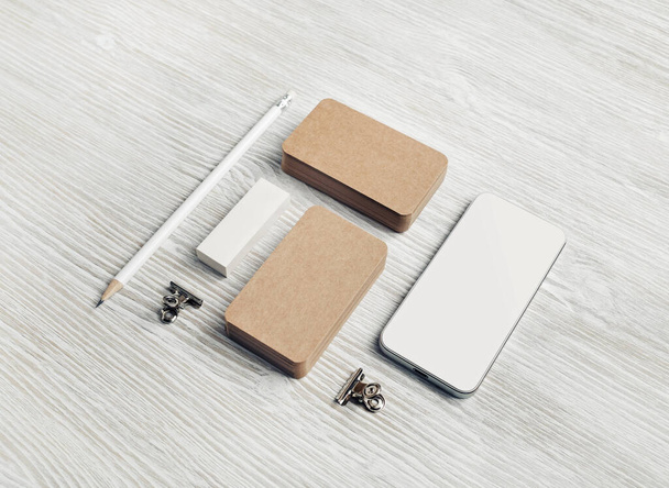 Prázdná šablona šablony papíru na pozadí stolu z lehkého dřeva. Kraft vizitky, smartphone, tužka a gumy. - Fotografie, Obrázek