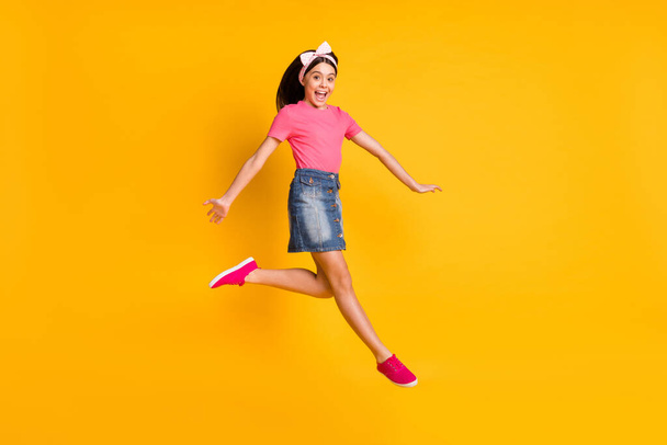 Photo of impressed shiny school girl wear pink t-shirt smiling jumping high isolated yellow color background - 写真・画像