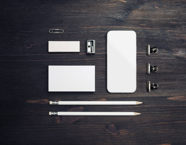 Smartphone a papírnictví: prázdné vizitky, tužky, gumy a ořezávátko na pozadí dřevěného stolu. Plocha. - Fotografie, Obrázek
