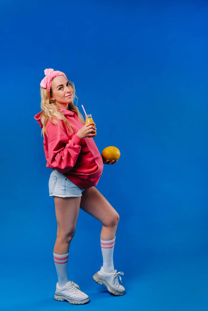 pregnant girl in pink clothes with a bottle of juice and a melon on a blue background. - Φωτογραφία, εικόνα