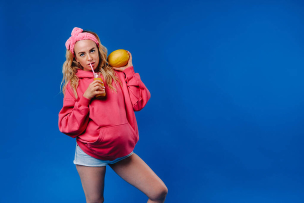 pregnant girl in pink clothes with a bottle of juice and a melon on a blue background. - Foto, immagini